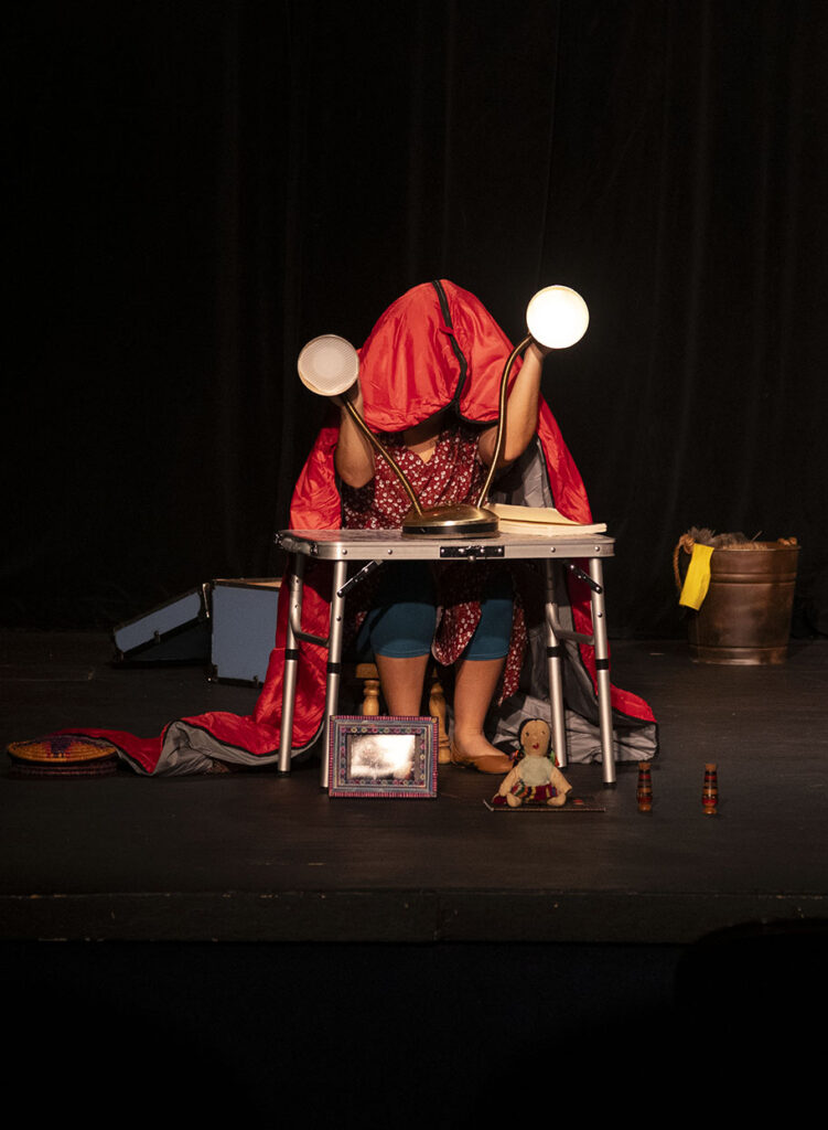 Belinda hides under her sleeping bag while manipulating Gustavo and Ernesto, two brass colored table lamps